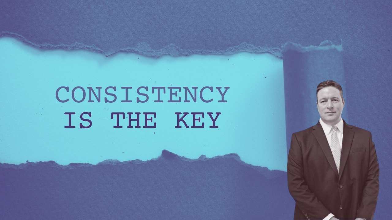 joe standing in front of a sign that says consistency is key