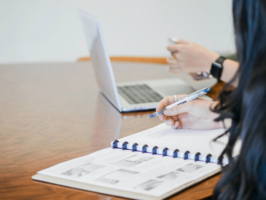 a person sitting a table with another person on a computer